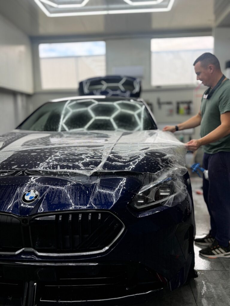 Aplikator układa przezroczystą folię PPF na masce BMW serii 1 2026
