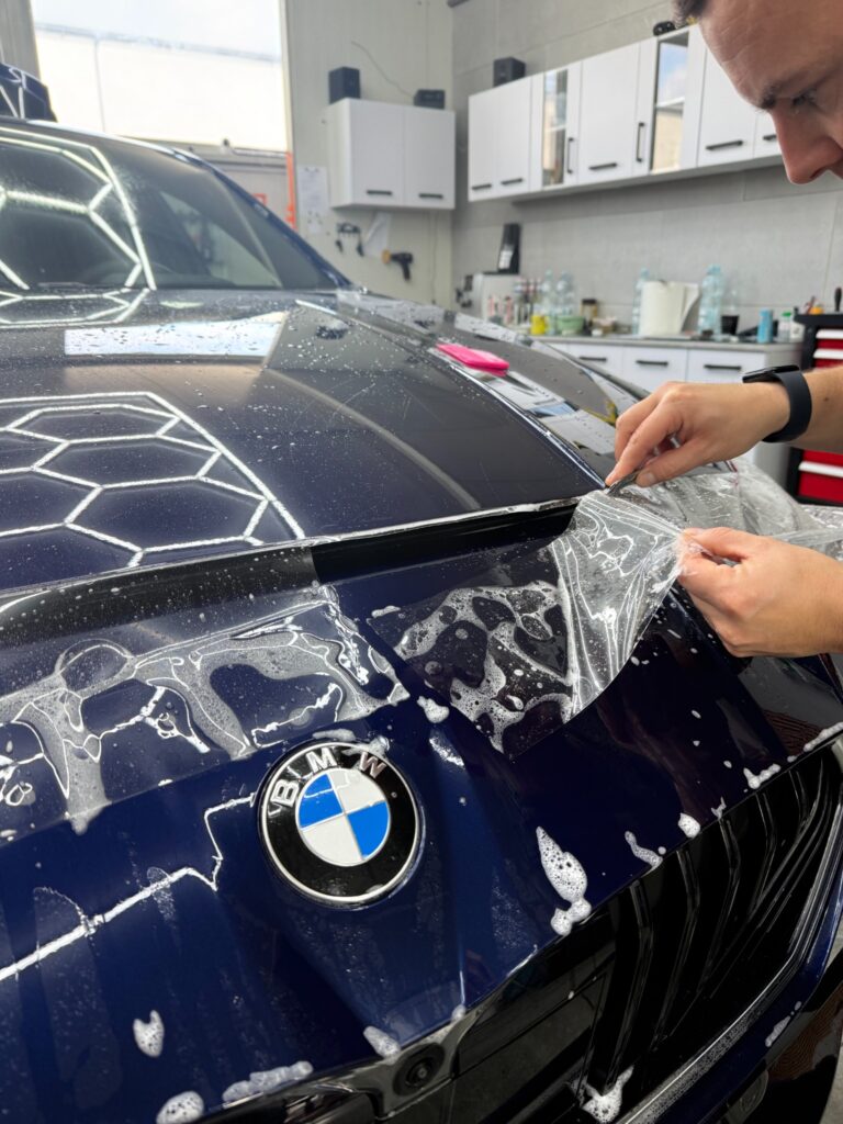 Zbliżenie na montaż bezbarwnej folii PPF na granatowej masce BMW serii 1