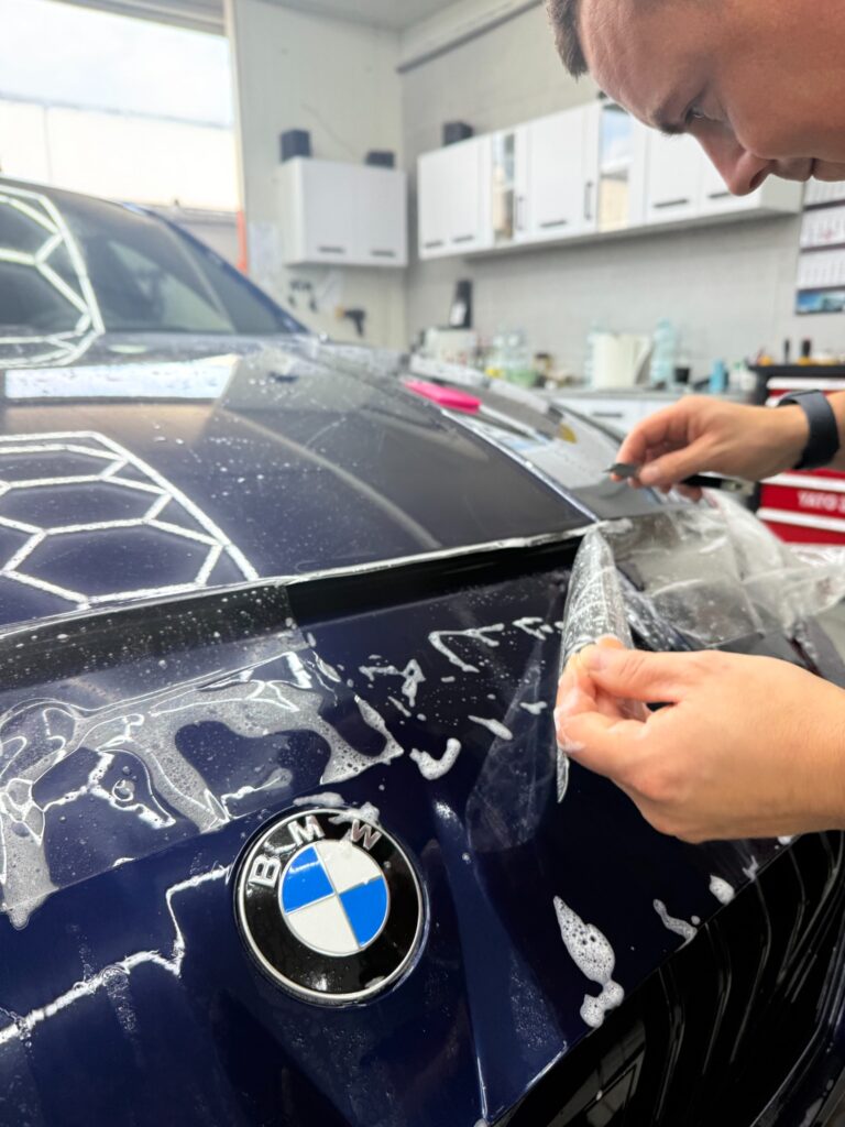Praca nad folią PPF przy przedniej krawędzi maski BMW serii 1