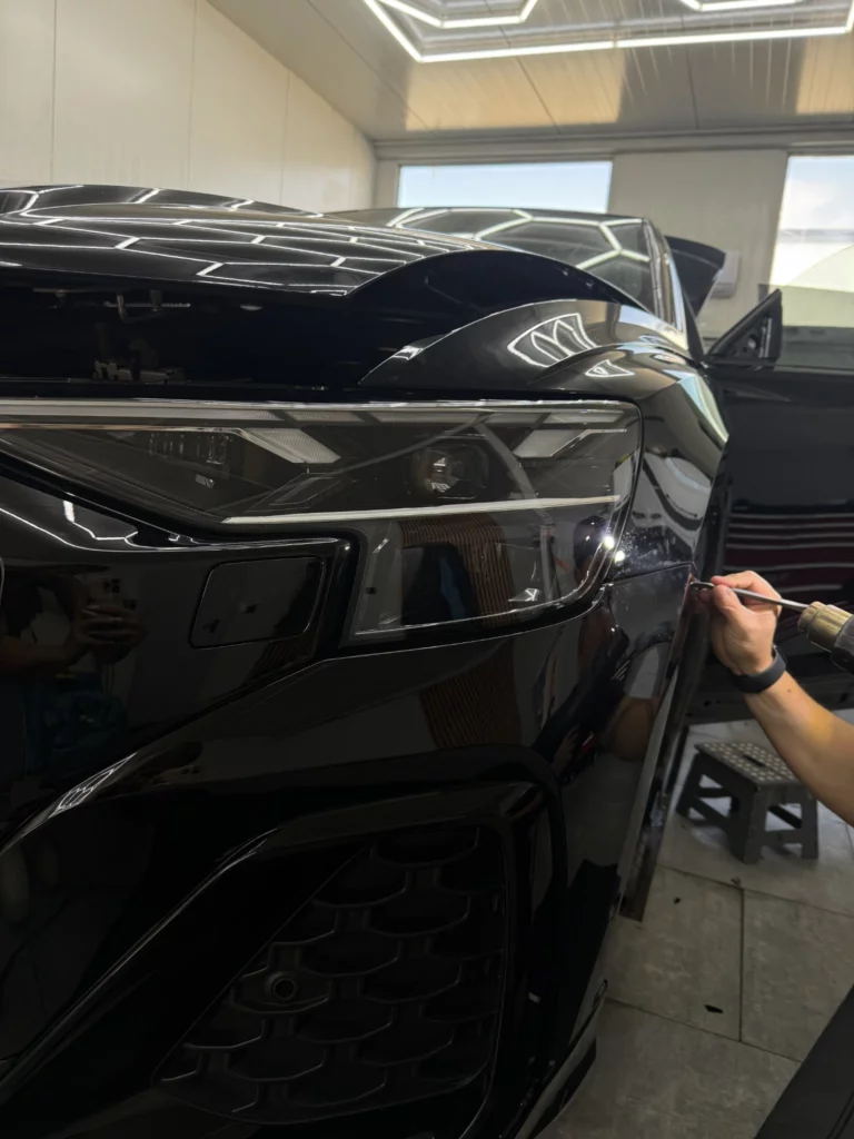 Praca przy folii na narożniku przedniego zderzaka Audi Q8 pod reflektorem