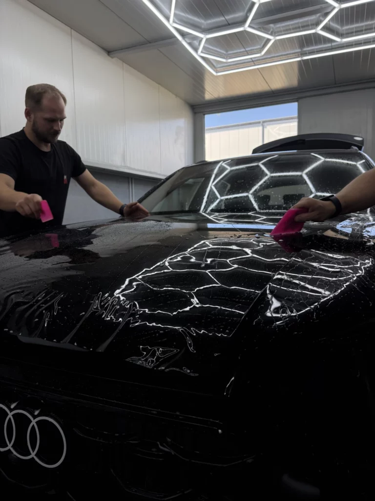 Dwóch instalatorów układa czarną folię na masce Audi Q8