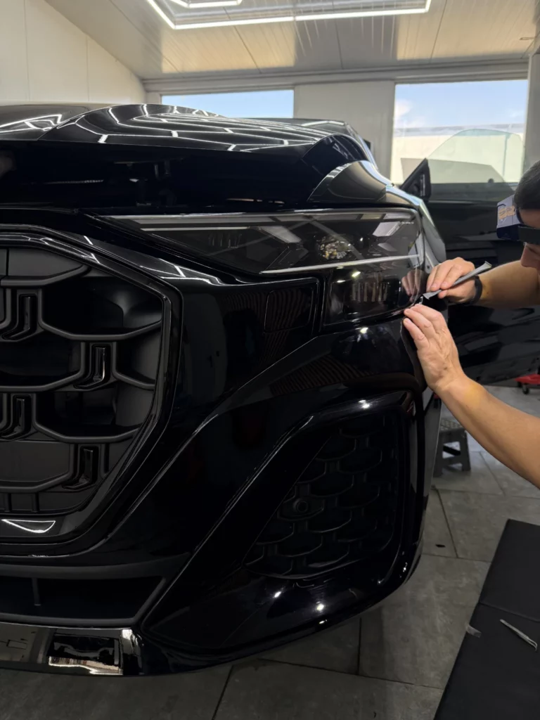 Instalator wykańcza folię na przednim zderzaku Audi Q8 obok grilla