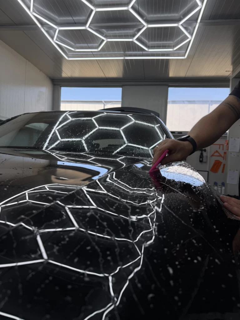 Aplikacja czarnej folii na masce Audi Q8 przy użyciu różowej rakli