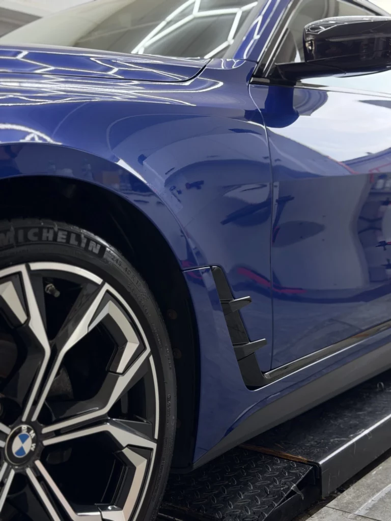 Przedni błotnik i drzwi niebieskiego BMW serii 4 z odbiciami światła
