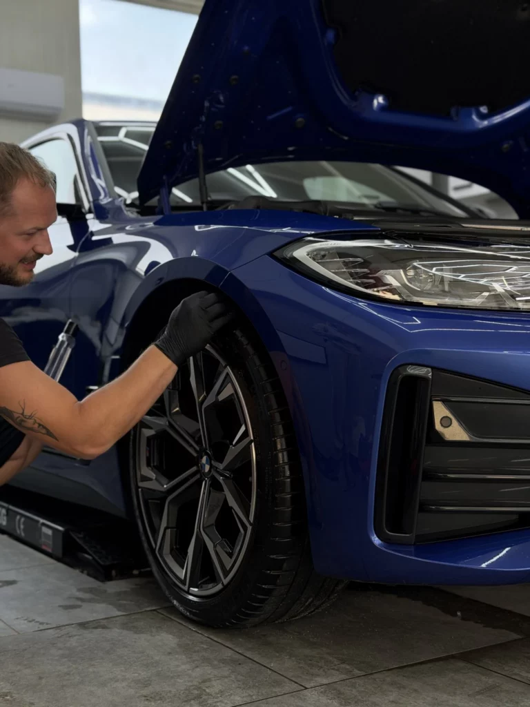 Instalator pracuje przy przednim nadkolu niebieskiego BMW serii 4