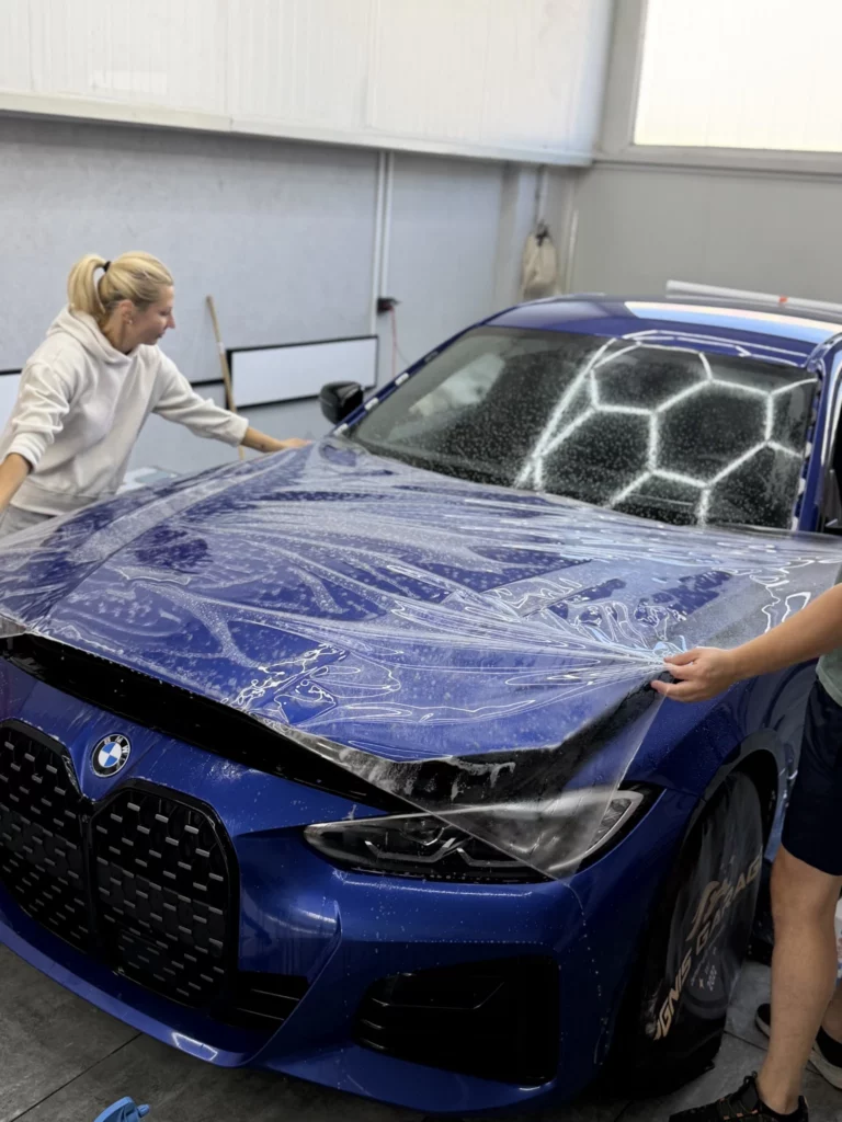 Zespół instalatorów układa bezbarwną folię PPF na masce BMW serii 4