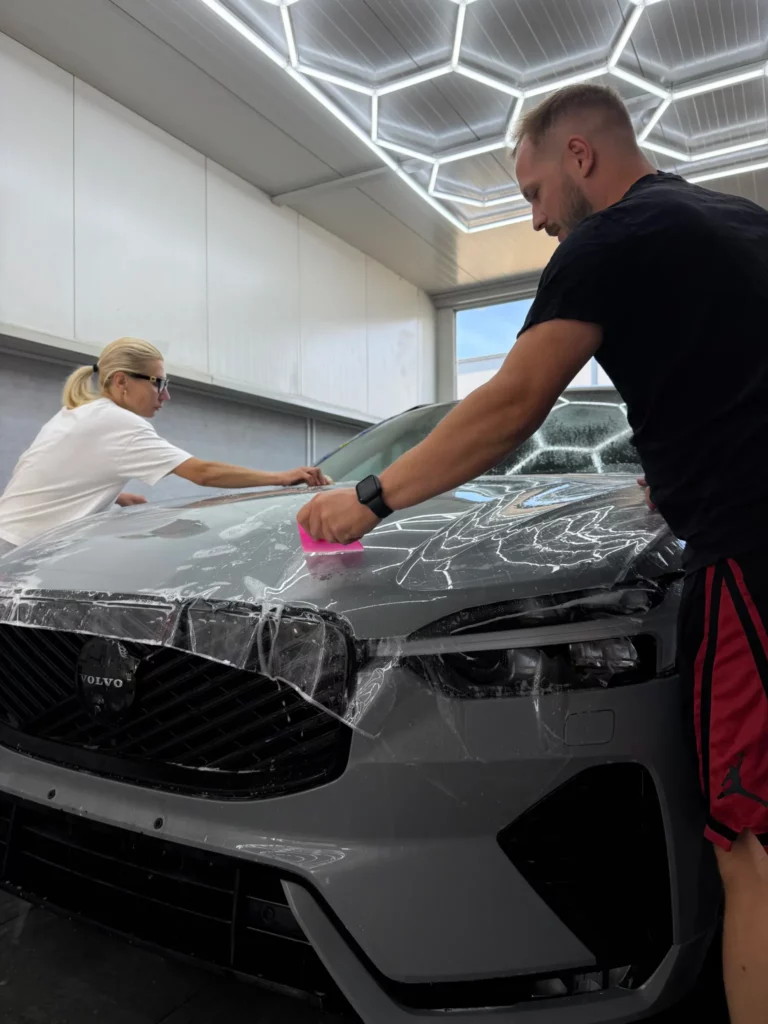 Dwóch instalatorów nakłada folię ochronną na maskę Volvo XC60 w IGNIS Garage
